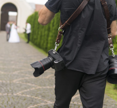 Professional wedding photographer takes pictures of the bride and groom in garden, the photographer in action with two cameras on a shoulder straps
